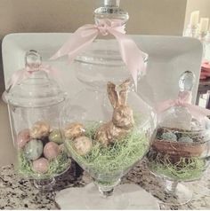 three glass vases filled with easter eggs and small bunny in them on a table