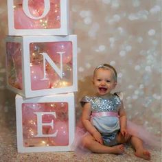 a baby sitting on the floor in front of three blocks that spell out the word one