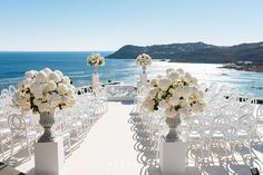 an outdoor wedding setup with white flowers and chairs overlooking the ocean in front of it