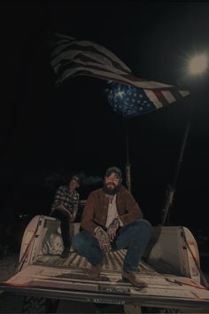 two men sitting in the back of a pickup truck with an american flag on it