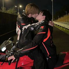 two people sitting on a red motorcycle kissing each other's foreheads at night