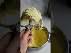 a hand holding a spoon with yellow food in it and another person peeling something off the bowl