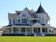 a large white victorian style house in the middle of a grassy area with trees and bushes