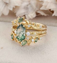 two gold rings with green and white stones on them, one has an oval stone surrounded by leaves