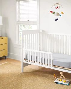 a white crib in a room with yellow dressers and window blinds on the windowsill