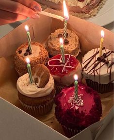 a box filled with lots of cupcakes covered in frosting and lit candles