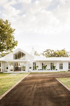 a large white house sitting on top of a lush green field next to a dirt road