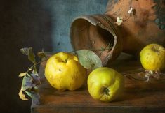 three yellow apples sitting on top of a wooden table next to a potted plant