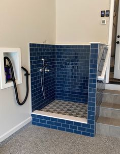 a blue tiled shower in a bathroom next to some steps and a phone on the wall