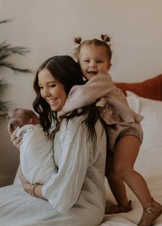 a woman holding a baby while sitting on top of a bed