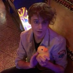 a young man holding a stuffed animal in his right hand while sitting on the floor