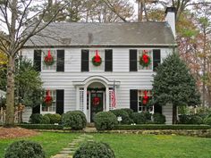 a white house decorated for christmas with wreaths on the front door and red ornaments hanging from the windows