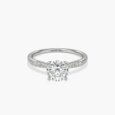 a white gold engagement ring with diamonds on the band and a round cut diamond in the center