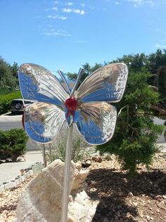 a blue and red glass butterfly sitting on top of a rock next to a tree