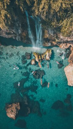 an aerial view of people swimming in the water near a waterfall and some rocks on the shore