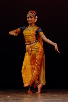 a woman in an orange and yellow dress is dancing with her arms out to the side