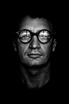 a man with glasses is looking at the camera in black and white, while he's staring straight ahead