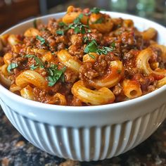 a white bowl filled with pasta covered in meat and sauce on top of a table