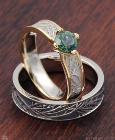 two wedding rings with one green stone in the middle