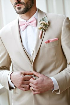 a man in a tan suit with a pink bow tie and boutonniere