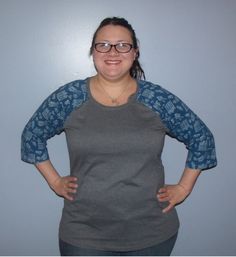 a woman standing with her hands on her hips wearing glasses and a gray shirt, smiling at the camera