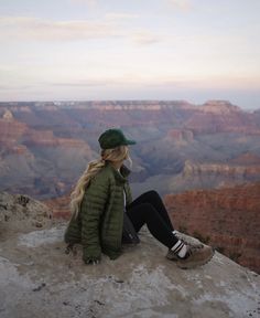 a woman sitting on the edge of a cliff looking at the grand canyon in the distance