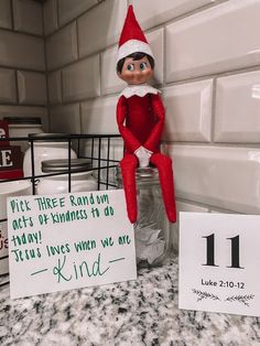 an elf is sitting on top of a mason jar next to two signs that read, pick three random out of happiness to do jesus loves when we are kind of kind