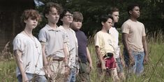 a group of young men standing next to each other in tall grass with trees in the background