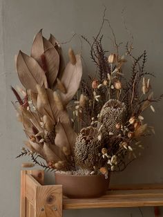 a vase filled with lots of dried flowers on top of a wooden shelf next to a wall