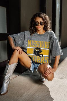 a woman sitting on the ground with her legs crossed and wearing a shirt that says mississippi tigers