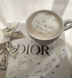 a cup of cappuccino on top of a dior book with ribbons