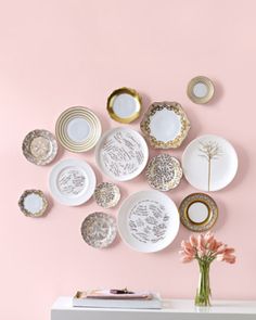 a white table topped with lots of plates on top of a pink wall next to a vase filled with flowers