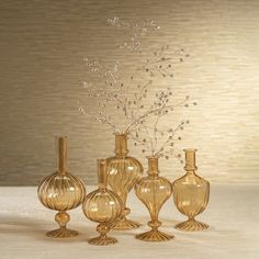 four glass vases with flowers in them on a white tableclothed surface next to a wall