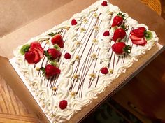 a large white cake with strawberries on top in a cardboard box sitting on a table