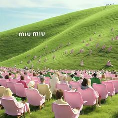 a large group of people sitting in pink chairs on top of a lush green hillside