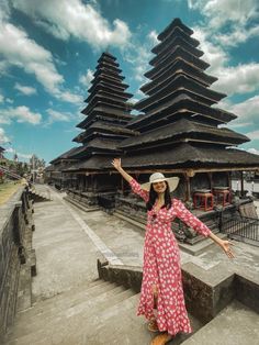 a woman wearing a hat standing in front of a tall building with pagodas on it