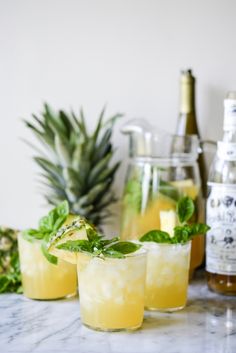 three glasses filled with drinks sitting on top of a counter next to pineapples