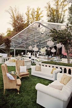 a group of couches and chairs sitting on top of a lush green field under a tent