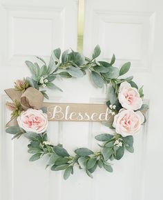 a white door with a wreath that says,'blessed'and pink flowers on it