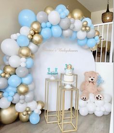 a teddy bear sitting in front of a cake and balloon arch with balloons on it