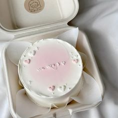 a white cake with pink frosting and hearts in a box on top of a bed