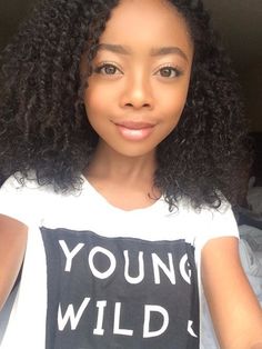 a woman with long curly hair wearing a young wild t - shirt and looking at the camera