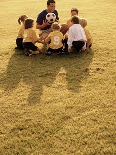 a man sitting on the ground with children holding a soccer ball