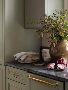 a vase filled with pink flowers sitting on top of a counter next to plates and bowls