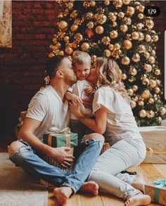 a man and woman sitting next to a christmas tree with presents in front of them