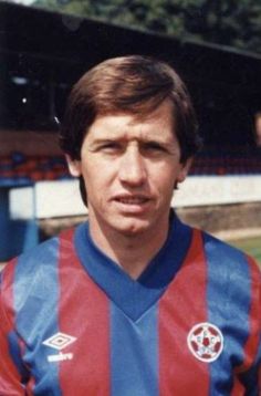 a man standing in front of a soccer field wearing a red and blue shirt with stripes on it