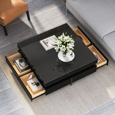 a black coffee table with drawers underneath it and flowers in a vase on the top