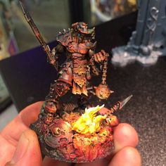 a person holding up a miniature figurine with flames in it's hands