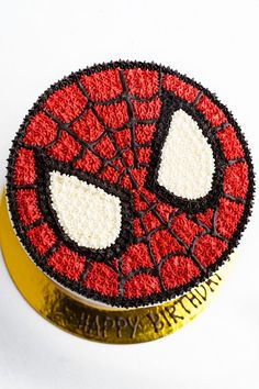 a spiderman cake is on top of a gold tin with white and black frosting