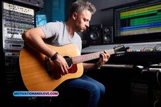 a man sitting in front of a mixing desk playing an acoustic guitar